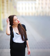 Portrait of a young stylish handsome long-haired woman in center city at sunset on blurred...