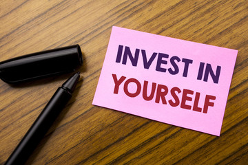 Word, writing Invest In Yourself. Business concept for Self Motivation Written on sticky note red paper, wooden background with pen. Note stick on the desk.