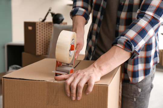 Young man packing moving box indoors, closeup