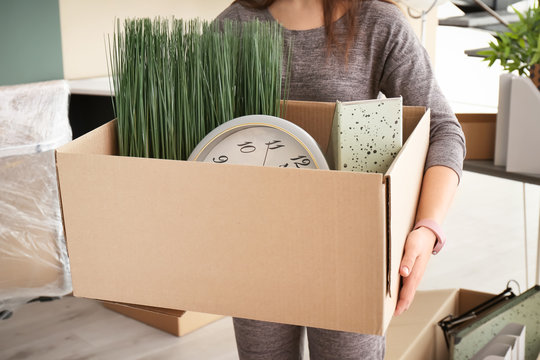 Young woman holding moving box with office stuff indoors, closeup