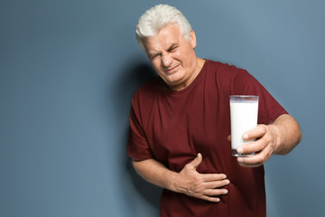 Mature man with dairy allergy holding glass of milk on color background