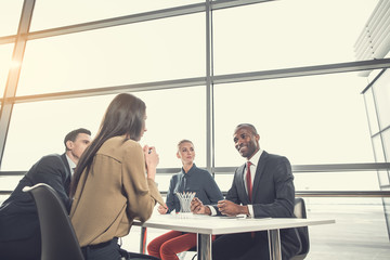 Low angle cheerful woman speaking with pleased colleagues while sitting at table in contemporary office. Positive partners during job concept