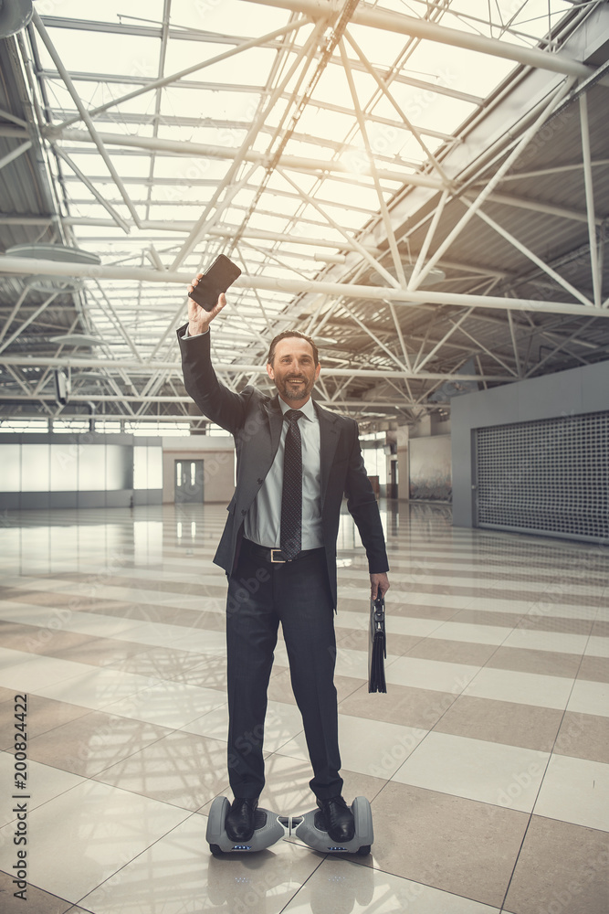 Poster full length portrait of beaming beaded employer gesticulating hands with cellphone while going on gi