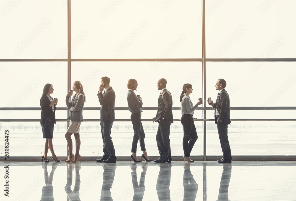 Poster full length outgoing colleagues drinking cups of delicious liquid while looking at window in break a