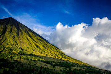 Green slopes of Gunung Inerie volcano with low clouds on the Indonesian island of Flores