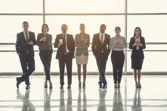 Full length portrait of dissatisfied colleagues drinking cups of liquid during break. They locating in lounge zone of business center. Discontented employees resting at job concept