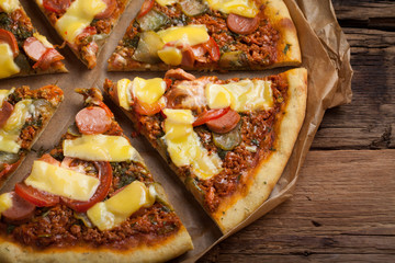 Homemade vegan pizza with tomatoes, cucumbers, vegan sausages and cheese on an old wooden table. Top view