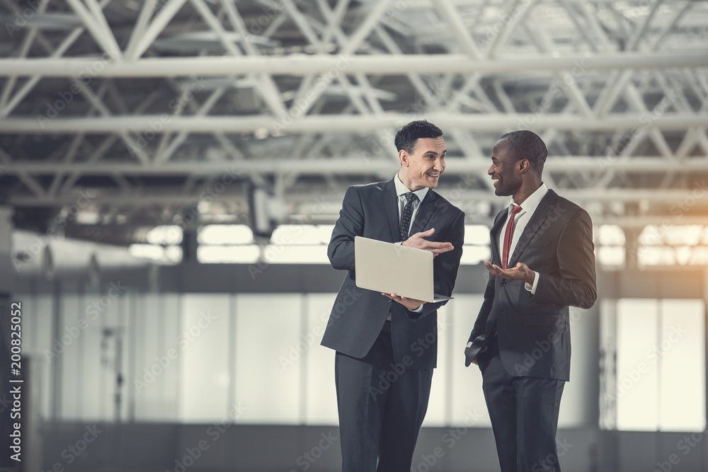 Poster side view beaming businessmen working with laptop while talking together. they gesticulating hands i