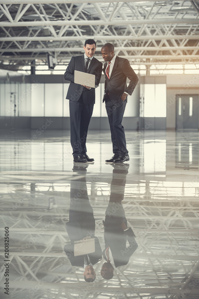Poster full length outgoing males looking at notebook computer while standing indoor. cheerful colleagues d