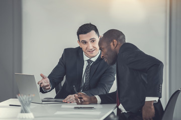 Smiling man talking with partner while gesticulating hand. Glad affiliate watching at screen of...