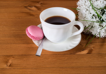 Cup of coffee and French macaroons and a white bouquet of flowers on a wooden background