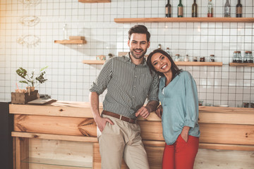 Portrait of joyful young man and woman dating in cozy cafeteria. They are standing near counter and laughing
