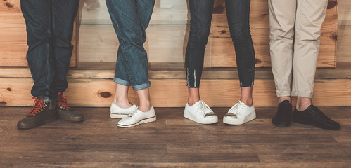 Close up of man and woman foot posing differently on flooring. Focus on their casual pants and shoes