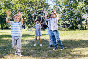 Adorable little children catching soap bubbles while spending warm summer day in public park illuminated with sunbeams