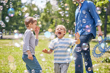 Portrait shot of cute little boy trying to catch soap bubbles with his mouth while having childrens...