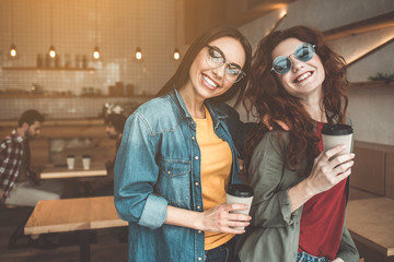 Waist up portrait of charming two female friends having fun in coffee shop. They are looking...