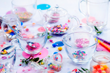Glass tea cups in the morning light. Birthday party concept with sprinkles, confetti, candies, macaroons and birthday candles. Colorful celebration concept
