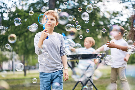 Group of little boys wrapped up in blowing colorful soap bubbles while gathered together at green public park