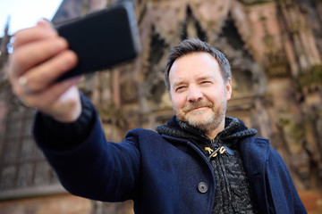 Middle age tourist making selfie mobile photo with famous Сathedral Notre Dame of Strasbourg on background