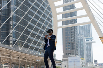 Young Asian businessman in a suit wear and virtual reality glasses who fighting boxing in the background of bangkok city,  the business district with high building dazzled