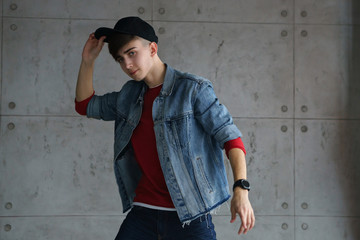 Obraz premium Teenager in red sweater and denim jacket dancing hip-hop with baseball cap. Dynamics and plastic movement of modern dance. Youth fashion.