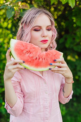 Beautiful young woman with pink hair enjoying watermelon