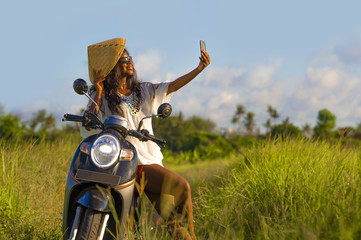 young attractive black afro American tourist woman in Asian traditional hat riding motorbike taking...