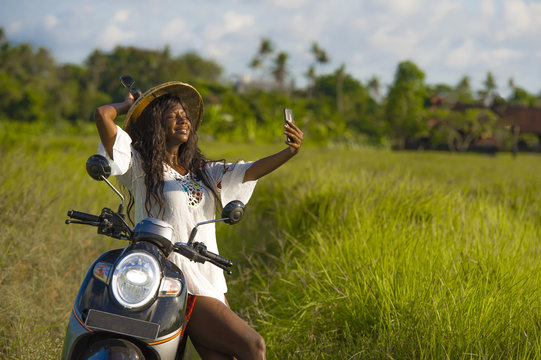 young attractive black afro American tourist woman in Asian traditional hat riding motorbike taking selfie photo with mobile phone smiling happy