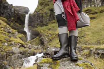 Closeup of black rain boots in front of Icelandic waterfall