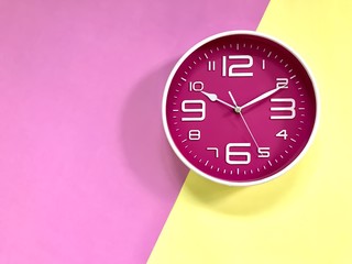 Closeup A deep pink wall clock set on pastel pink and yellow background. Theme of Working business time .The concept of " The time is going on." Top view with Selective focus. Copy space.