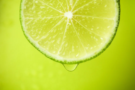 Close-up of a slice of lime, a drop of water falls. The fruit gives off freshness and juice filling.