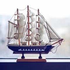 The model of a sailing ship stands on a misted window. The concept of travel. Dreams of a vacation
