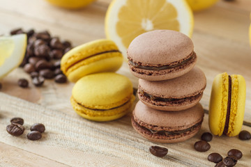 Obraz na płótnie Canvas Yellow and brown french macarons with lemons and coffee beans on the wooden board