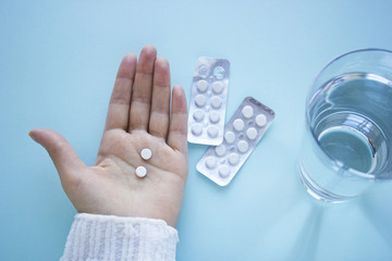 Woman hand holds two tablets with glass of water on  blured blue background. Health and medical concept treatment of diseases. Woman drinks tablets. Top view.