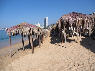 Beauty exotic bamboo huts on sandy beach at bay of ACAPULCO city in Mexico with skycraper and waves...