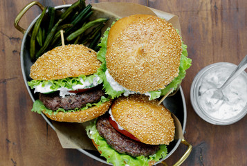Burgers with beef cutlets and fried bean pods are served in a frying pan on wooden table with sauce, top view