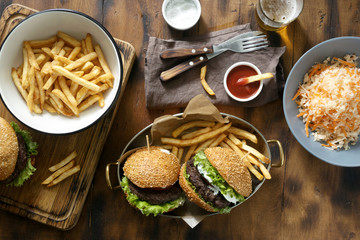 Delicious outdoor table with burger, french fries and salad on wooden table with beer, top view. Outdoors food Concept