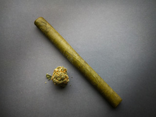 A marijuana bud and a cigarillo are isolated on a gray background.