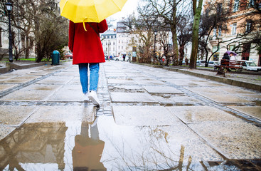 woman in red coat with yellow umbrella walk by street in rainy weather. copy space