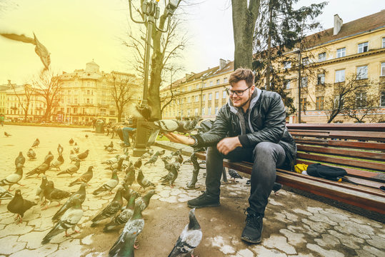young man feed doves in city park.