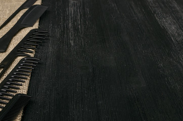 Set of black plastic hair comb on sackcloth burlap background with black wooden surface copy space. Barber hairdresser work.desk table concept.