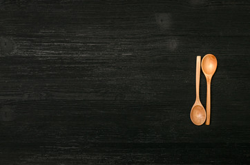 Two wooden spoon on black wood surface of kitchen table background with copy space. Top view.