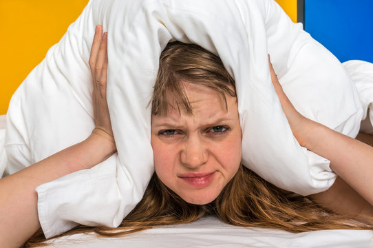 Woman in bed covering ears with pillow because of noise
