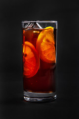One-color, red, brown, transparent cocktail with ice cubes and lemon slices, orange. Side view. Isolated black background. Drink in a glass glass for the menu restaurant, bar, cafe
