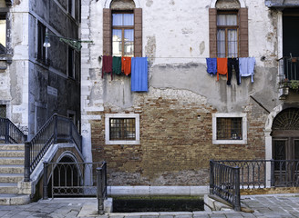 Fototapeta na wymiar Typical old Venetian facade made of red bricks and cement with colorful clothes outside the windows above a traditional canal with a dock for the gondola