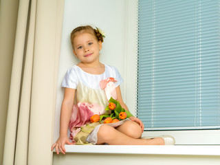 A little girl is sitting on the windowsill with a bouquet of tul