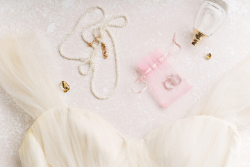 Flatlay with bridal dress and accessories on creamy pink background with text space