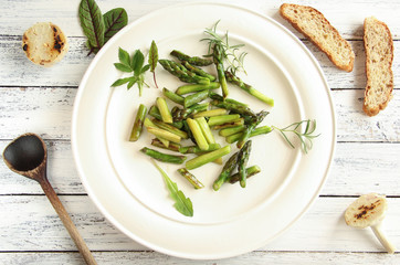 frischer grüner Spargel gebraten Salat Spargelsalat Teller Brot overhead weiß Brett 