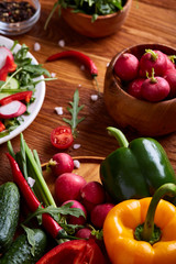 Fresh red radish in wooden bowl among plates with vegetables, herbs and spicies, top view, selective focus.