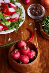 Fresh red radish in wooden bowl among plates with vegetables, herbs and spicies, top view, selective focus.